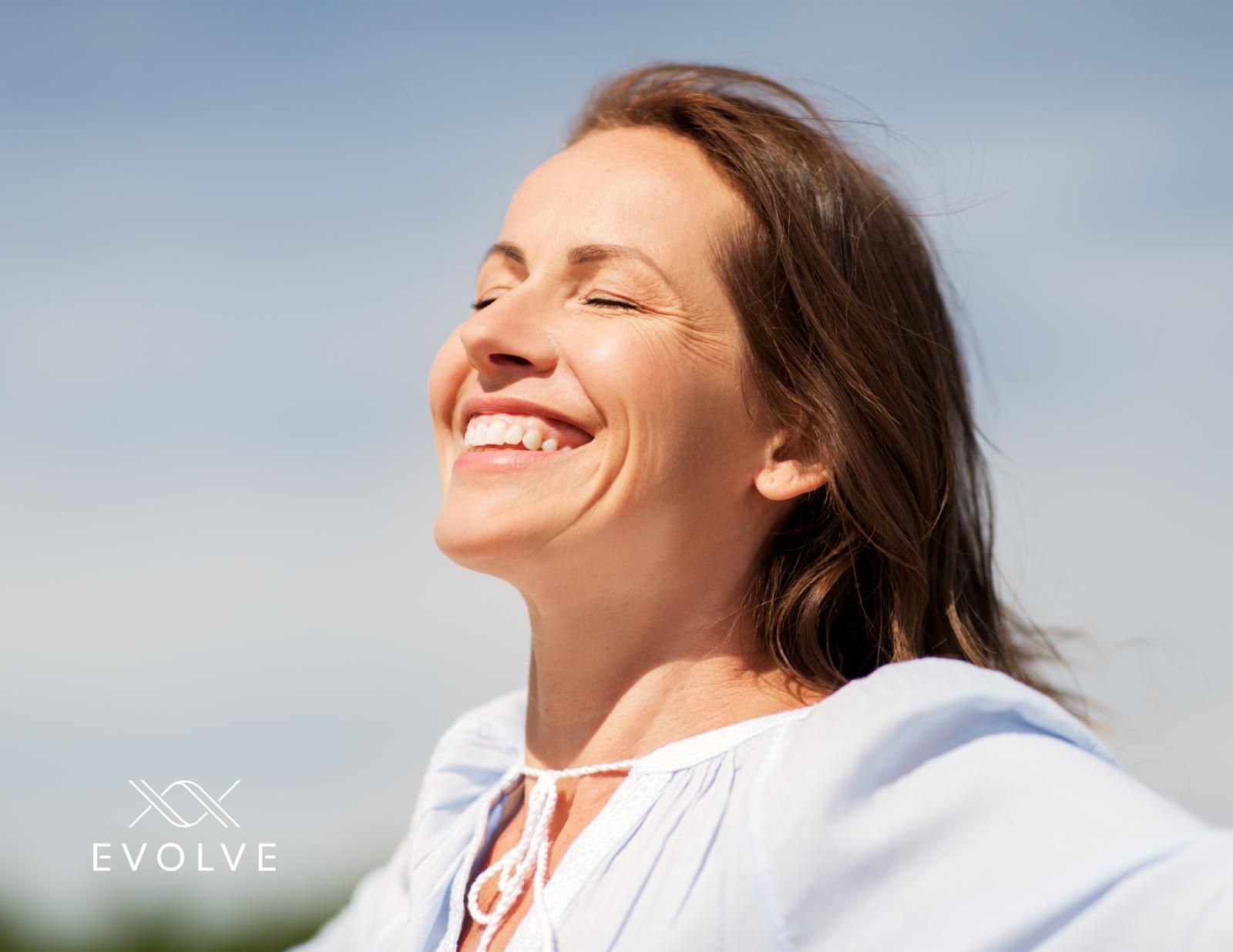 A smiling woman with eyes closed, standing outdoors under a clear blue sky, radiating peace and confidence. Evolve logo in the corner.